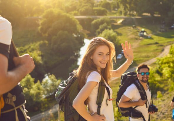 Group of happy friends with backpacks walking down hiking trail on sunny day in summertime